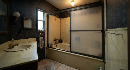 Before image of dark 1990s Conway bathroom with high step-over acrylic garden tub, cracked grout lines, frosted sliding